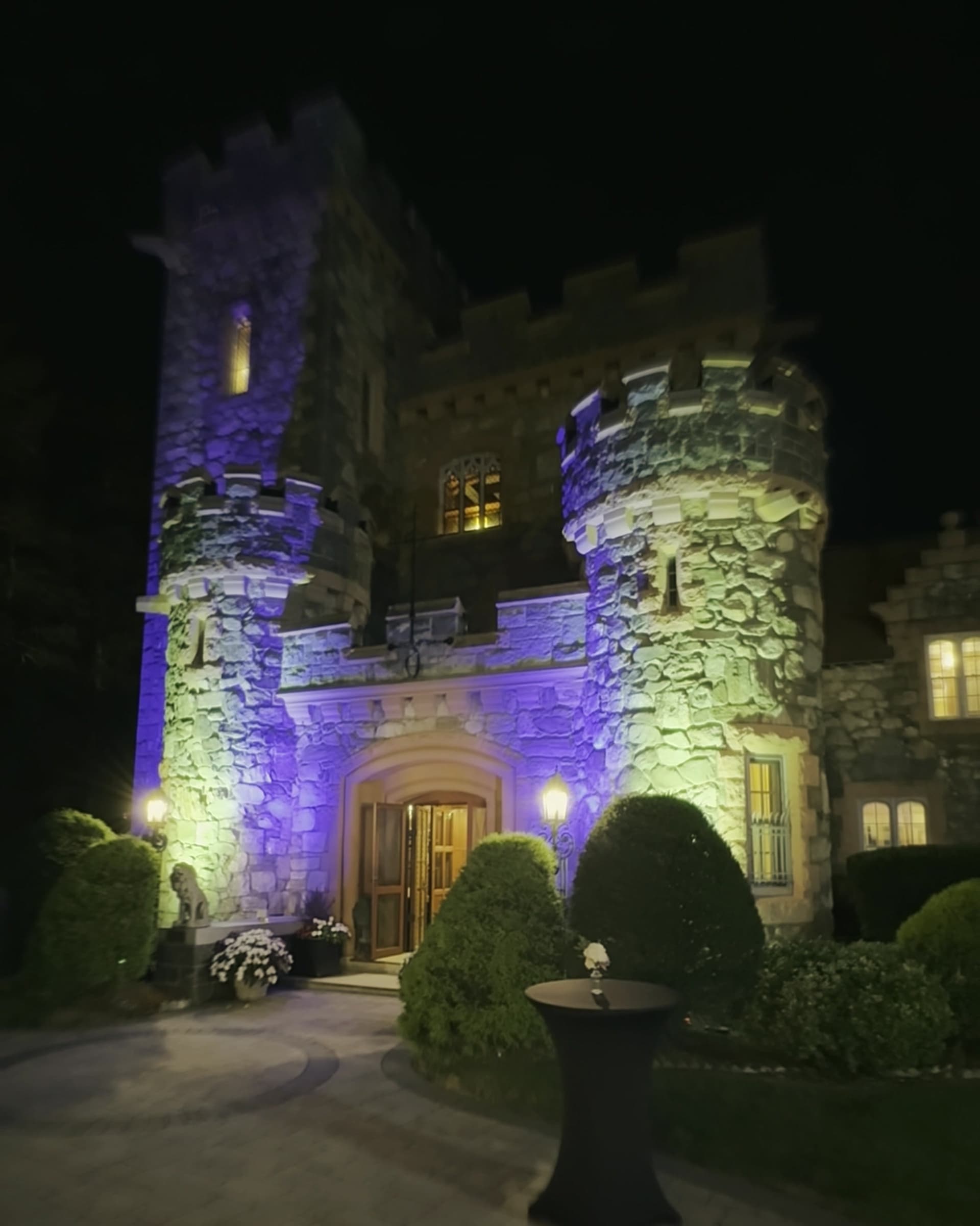 A stone castle venue uplit in blue and violet at night, a cocktail table by the lit entrance